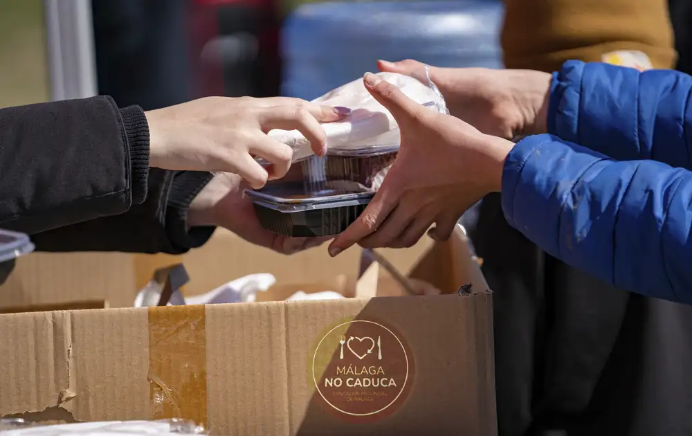 Manos entregando comida en caja con logo Málaga No Caduca