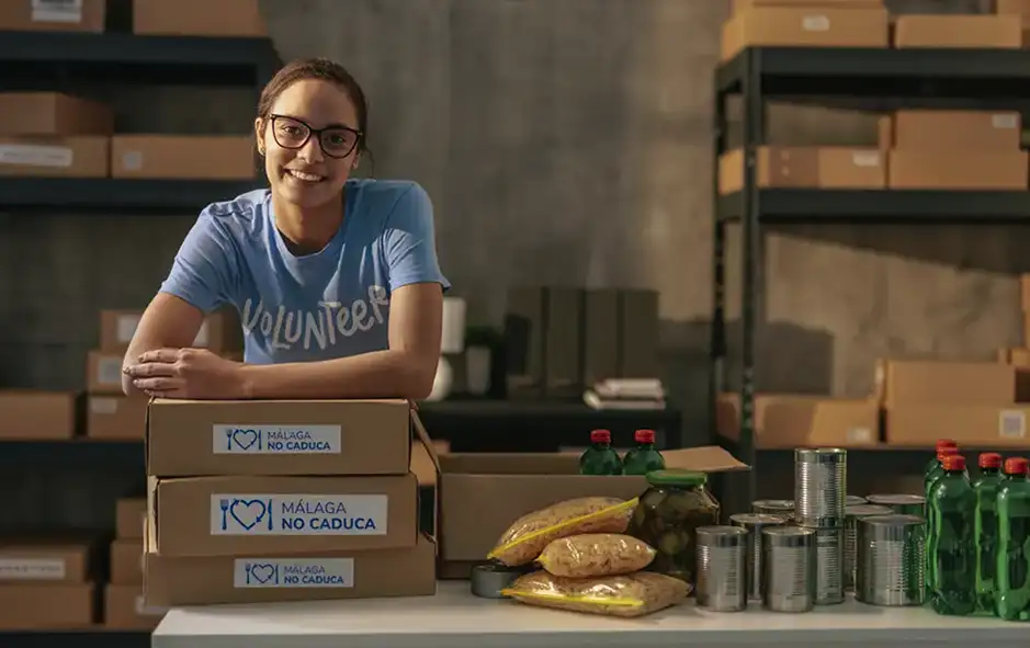 Voluntaria sonriendo junto a cajas de alimentos Málaga No Caduca para distribución